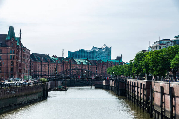 Hamburg, Germany - August 23, 2019: Old warehouses converted into offices and flats next to a canal and the Elbphilharmonie, Elbe Philharmonic Hall, with people around in HafenCity, Hamburg, Germany 