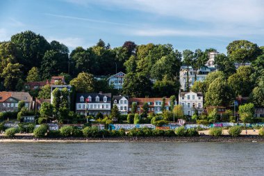 Hamburg, Almanya - 22 Ağustos 2019: Yazın Hamburg, Almanya 'daki Elbe nehri kıyısındaki bir plajda ve lüks evlerde yaşayan insanlar 