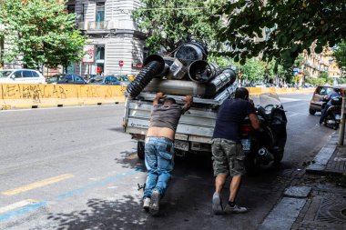 Napoli, İtalya - 9 Eylül 2019: Biri eski Napoli, İtalya 'da bir caddede cep telefonuyla konuşurken, iki adam hurda dolu hasarlı bir minibüsü itiyor