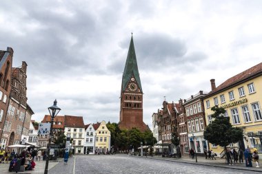 Lunenburg, Almanya - 17 Ağustos 2019: Vaftizci Yahya Kilisesi veya St. Johannis ve Am Sande, tipik kasaba evleri ve etrafındaki insanların bulunduğu alışveriş caddesi, Aşağı Saksonya, Almanya