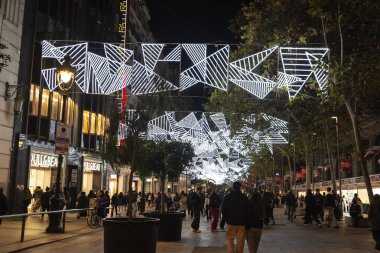 Barselona, İspanya - 25 Kasım 2025: Geceleyin sokakta asılı duran Noel ışıkları süslemesi Portal de Angel Bulvarı, Barselona, Katalonya, İspanya 'da insanlar tarafından aydınlatıldı