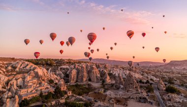 Kapadokya, Türkiye - 07 Ekim 2019 - Turistlerle dolu balonlar eski köyün konilerinin üzerinde gün doğumunda yüzüyor