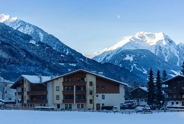Güneş karla kaplı dağların üzerinde parlarken aşağıdaki kulübe dağların gölgesinde.