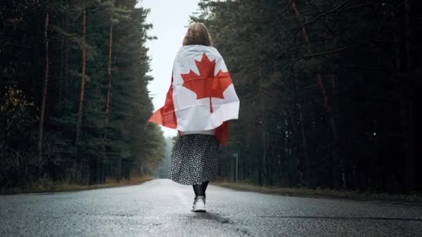 Dziewczyna w białym swetrze i spódnicy chodzi przez las trzymając flagę Kanady — Wideo stockowe