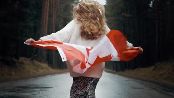 Dziewczyna w białym swetrze i spódnicy biegnie przez las trzymając flagę Kanady — Wideo stockowe