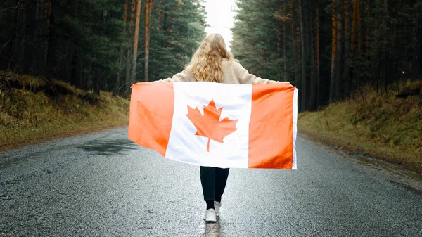 Ragazza cammina attraverso la foresta con la bandiera del Canada. Vista posteriore Fotografia Stock