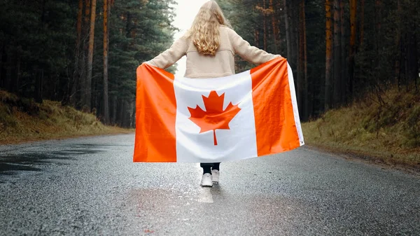 Menina caminha pela floresta segurando a bandeira do Canadá. Visão traseira — Fotografia de Stock