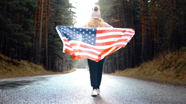 stock image Girl walks through the forest holding the flag of USA. Back view