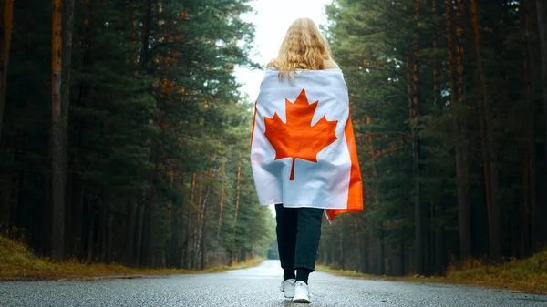 Ragazza cammina attraverso la foresta con la bandiera del Canada. Vista posteriore Foto Stock Royalty Free