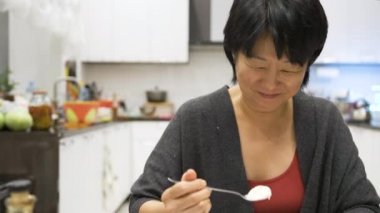 Evde dondurma yiyen Asyalı kadın. Gülümsüyor