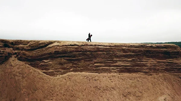 Una chica en overol y una tabla de snowboard está caminando sobre una roca en verano. —  Fotos de Stock