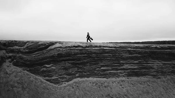 Una chica en overol y una tabla de snowboard está caminando sobre una roca en verano. —  Fotos de Stock