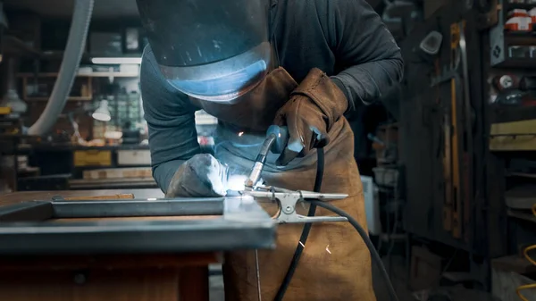 Metal parçaları lehimleyen maske ve eldiven giyen bir işçi.