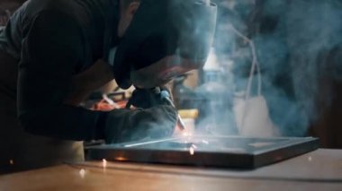 Metal parçaları lehimleyen maske ve eldiven giyen bir işçi.