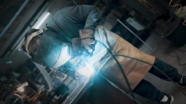 Metal parçaları lehimleyen maske ve eldiven giyen bir işçi.