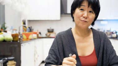 Evde dondurma yiyen Asyalı kadın. Gülümsüyor