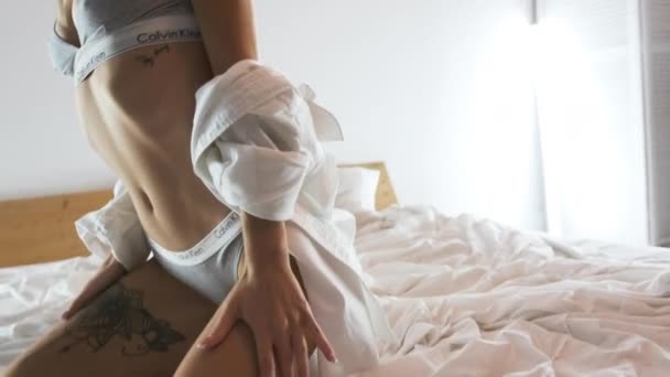 ТОМСК, РОССИЯ - 16 августа 2020 года: Сексуальная блондинка в нижнем белье и рубашке Calvin Klein на кровати. Портретная съемка — стоковое видео