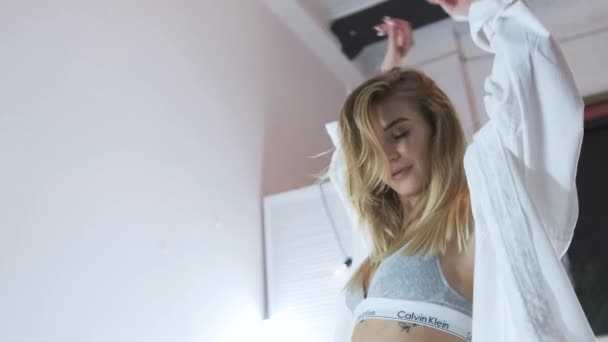 ТОМСК, РОССИЯ - 16 августа 2020 года: Сексуальная блондинка в нижнем белье и рубашке Calvin Klein на кровати. Портретная съемка — стоковое видео