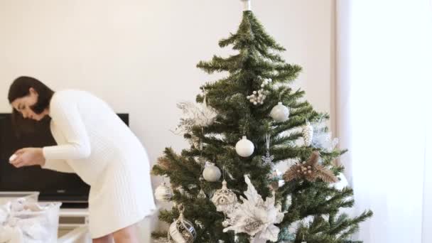 Belle fille brune dans une robe blanche décore le sapin de Noël avec des jouets à la maison — Video