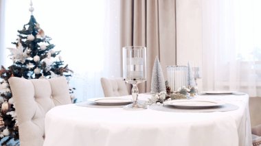 Beyaz elbiseli bir kız Noel masasında tabak servisi yapıyor. Kutlama tablosu ayarları