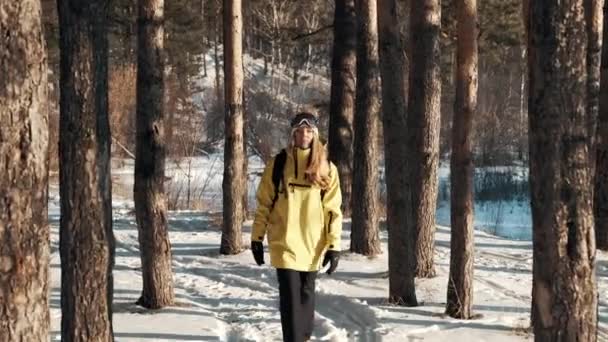 Dziewczyna w żółtej kurtce z plecakiem i maską snowboardową spaceruje po lesie. — Wideo stockowe