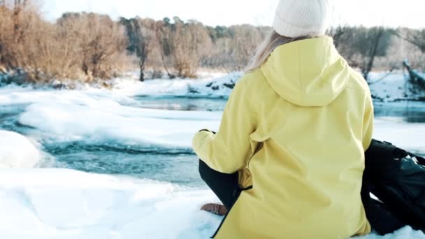 Gadis itu duduk di posisi teratai di musim dingin di hutan dan melihat sungai — Stok Video
