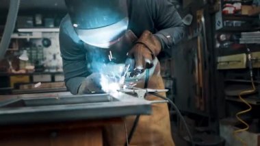 Metal parçaları lehimleyen maske ve eldiven giyen bir işçi.