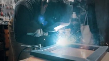 Metal parçaları lehimleyen maske ve eldiven giyen bir işçi.