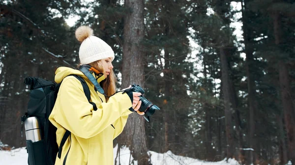 Девушка с рюкзаком и желтым анораком фотографирует пейзаж на профессиональную камеру — стоковое фото