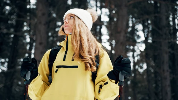 Девушка в белой шляпе в лесу с рюкзаком и пешеходными палками зимой. Вид спереди. Закрыть Лицензионные Стоковые Фото