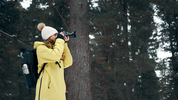 Een meisje met een rugzak en een gele anorak fotografeert het landschap op een professionele camera — Stockfoto