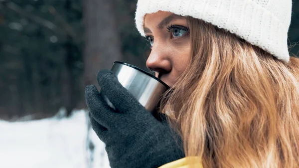Een meisje in een geel jasje drinkt 's winters thee uit een thermoskan in het bos — Stockfoto