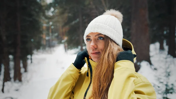 Menina em uma jaqueta amarela coloca um capuz na floresta no inverno — Fotografia de Stock