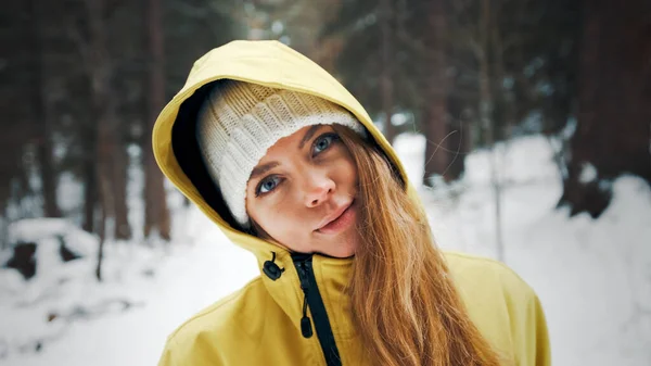 Meisje in een geel jasje en een hoodie glimlacht vooruit in de winter in het bos — Stockfoto