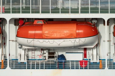Bir yolcu gemisinin yan tarafına monte edilmiş turuncu ve beyaz cankurtaran botu.