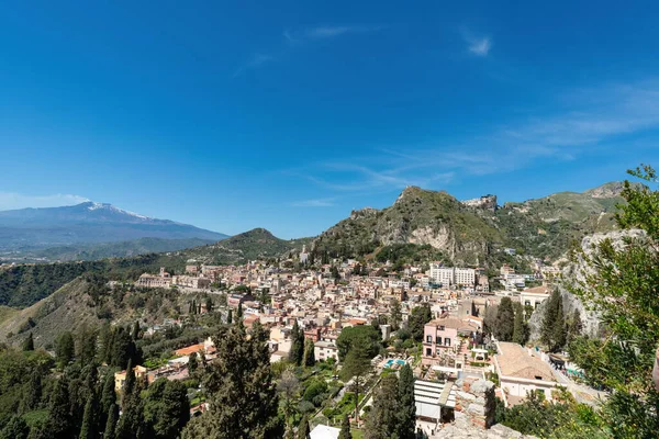 Yeşil tepelerdeki Taormina kasabasının panoramik manzarası. Arka planda Etna Yanardağı, Sicilya, İtalya