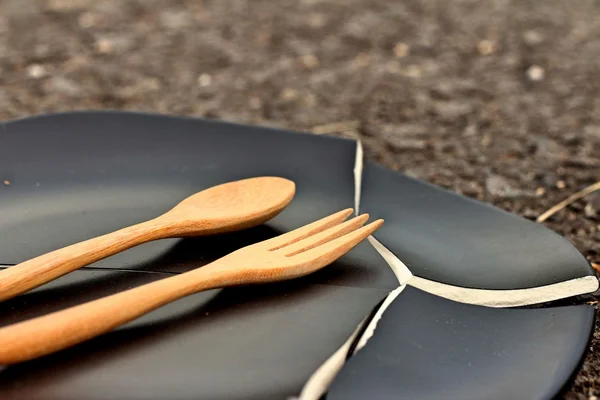 Spoon and fork on a crack  black plate. — Stock Photo, Image