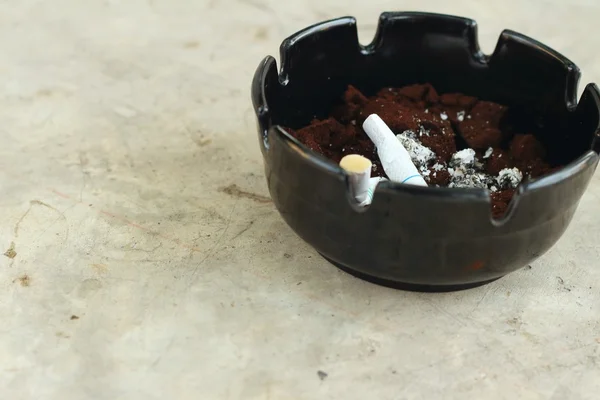 Cigarette in the ashtray on the cement floor. — Stock Photo, Image