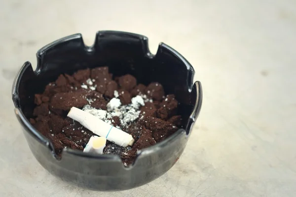 Cigarette in the ashtray on the cement floor. — Stock Photo, Image