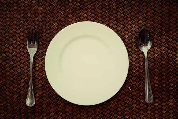 Bílý talíř, nůž a vidlička na ubrousek na dřevěné pozadí — Stock fotografie