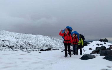 Bir grup dağcı taşların arasından karla kaplı bir patika boyunca yürüyorlar. Dağ tırmanışı. Klyuchevskoy volkan parkında gezinti. Kamçatka Yarımadası 'na git.