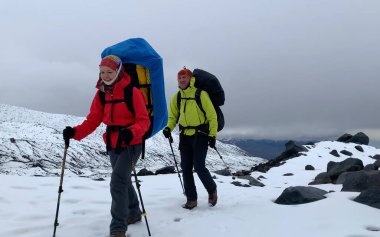 Büyük sırt çantaları ve yürüyüş direkleriyle iki dağcı karlı patika boyunca yürüyor. Dağ tırmanışı. Klyuchevskoy volkan parkında gezinti. Kamçatka Yarımadası 'na git..