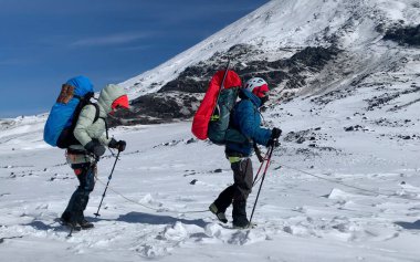 Büyük sırt çantaları ve yürüyüş direkleri olan birkaç dağcı desteler halinde yürür. Dağ tırmanışı. Klyuchevskoy volkan parkında gezinti. Kamçatka Yarımadası 'na git..