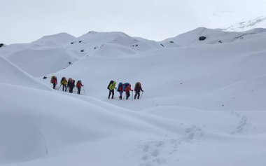 Büyük sırt çantaları ve yürüyüş direkleriyle birkaç dağcı karlı dağlarda yürüyorlar. Dağ tırmanışı. Klyuchevskoy volkan parkında gezinti. Kamçatka Yarımadası 'na git..