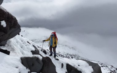 Kaskla tırmanan ve buz baltasıyla bir dağın yamacında duran bir adam. Dağ tırmanışı. Klyuchevskoy volkan parkında gezinti. Kamçatka Yarımadası 'na git..