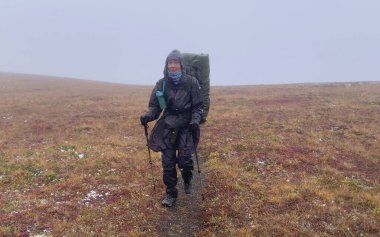 Büyük bir sırt çantalı bir kadın turist, sonbahar tundrası boyunca karda yürüyor. Dağ tırmanışı. Klyuchevskoy volkan parkında gezinti. Kamçatka Yarımadası 'na git.