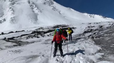 Kamçatka 'daki büyük bir karlı volkanın arka planına karşı büyük sırt çantaları ve yürüyüş direkleriyle bir grup donmuş turist. Kamçatka Yarımadası 'na git..