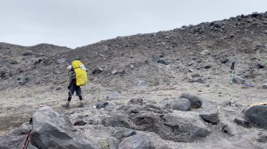Büyük sırt çantalı yorgun bir turist Kamçatka 'nın kayalık alanlarında yürüyor. Klyuchevskoy volkan parkında gezinti. Kamçatka Yarımadası 'na git..