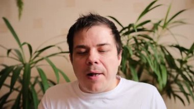 Beyaz tişörtlü hoş bir adam bir çeşit yemek çiğniyor. Genç adam bir dilim pizza alır. Arka planda yeşil bitkiler.