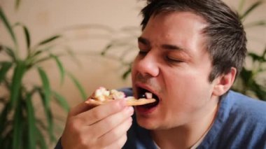 Adam büyük bir zevkle tatlı bir pizzaya bakıyor. Genç adam elma parçaları, böğürtlen, badem dilimleri ve yoğunlaştırılmış sütle bir parça tatlı turta alır ve onu zevkle çiğner. Yakın plan..